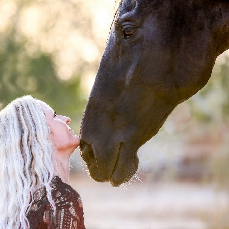 White-haired woman kissing a horse's muzzle.