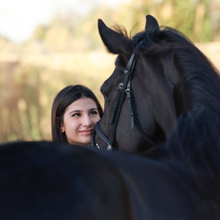 Woman smiling with a dark horse outdoors.